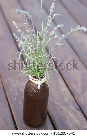 Painted glass bottle with lavender flowers and sprigs with twine around bottle on wooden table rustic table decor centerpiece top view