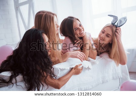 Cute smiles. Joyful girls in the nightwear lying on the bed in white room and have celebration.