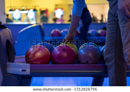 A close-up of a row of bowling balls in a bowling alley. Man taking balls to bow.
