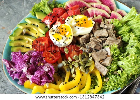 keto diet buddha bowl- salmon, avocado, boiled beef, watermelon radish, egg, salad greens, tomatoes. a bowl of nutrition rich in proteins and fats. sprinkle with oil, season with sunflower seeds