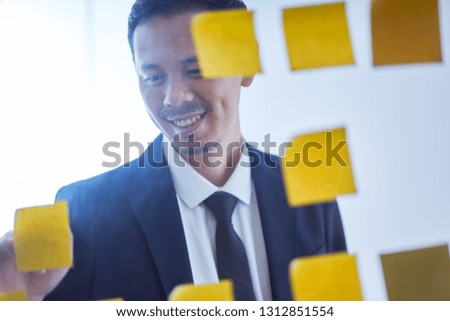 Asian businessman stand in glasses board with stickers and writing ideal , brainstorming concept .