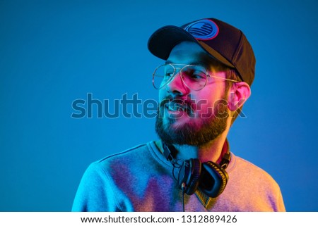 Enjoying his favorite music. Happy young stylish man in sunglasses with headphones smiling while standing against blue neon background