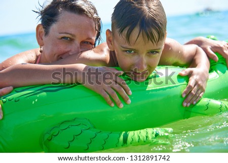 HAPPY SON AND MOM SWIM IN THE SEA ON INFLATED TOY CROCODILE IN THE SEA