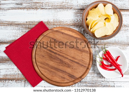 spicy red chilli potato chips and empty board on a wooden table