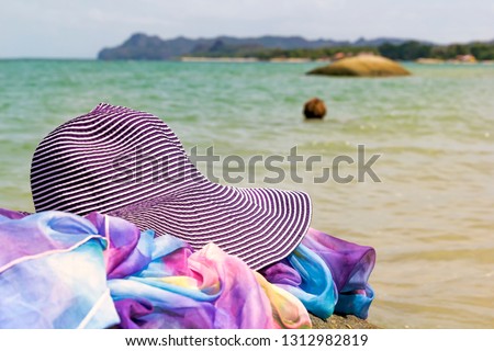 straw hat and pareo lie on a stone against the background of a woman’s head submerged in the sea on a sunny day