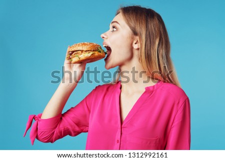 Beautiful blonde in a pink shirt eats a hamburger 
