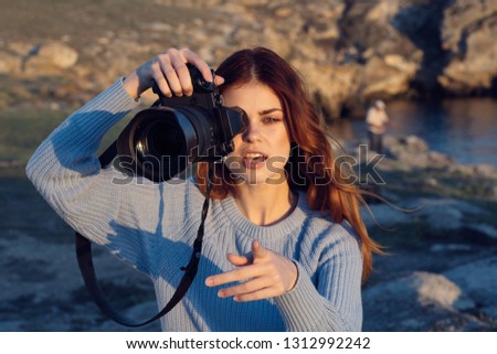 A woman with a camera on the banks of a river in the mountains is photographing nature 