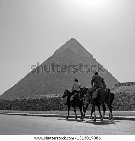 People riding horses at desert near the Great Pyramid of Giza (also known as the Pyramid of Cheops) in Egypt. Black and white photography