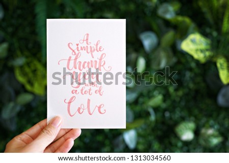 Hand holding card with modern calligraphy text "A simple thank you with a lot of love"                                   