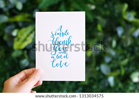 Hand holding card with modern calligraphy text "A simple thank you with a lot of love"                        