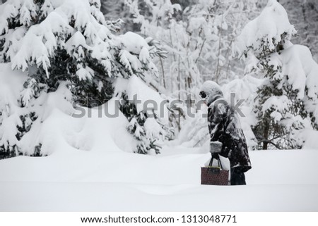 An elderly woman with a bag goes heavy in the snow and snowdrifts