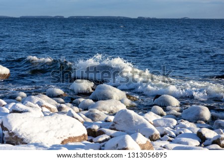 Frozen sea with snowy shores in Finland. Winter waves hitting the coast on a freezing cold sunny day.