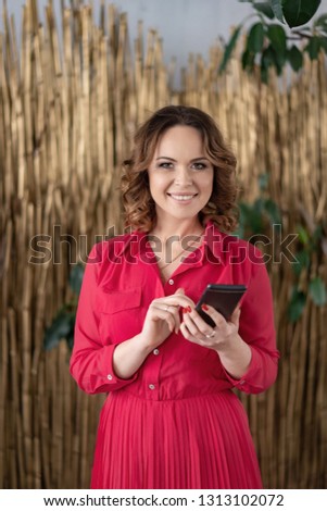 Young beautiful, business woman in a red coral dress is standing, confident, determined look into the camera with the phone in hand