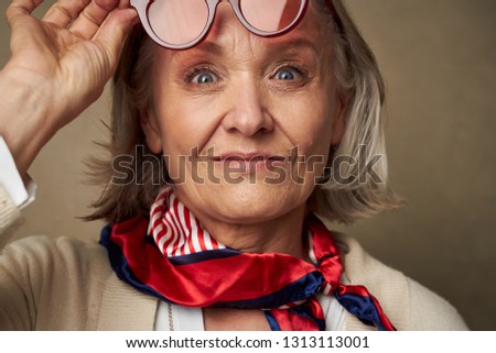 Cheerful pretty elderly woman. In a beige sweater, holding her hand near her face, close-up face