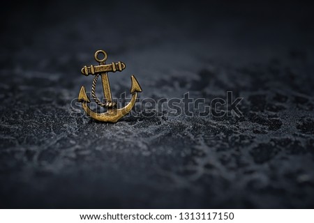 Metallic anchor close up on abstract black background. necklace of small bronze anchor. symbol of sailors, reliability, confidence. naval, pirates, travel concept. element for design. copy space