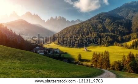 Wonderful nature Landscape. The greenery hills and small village with Alpine Mountain in background Val di Funes, Trentino Alto Adige, Italy. Odle on the background and Santa Magdalena Village