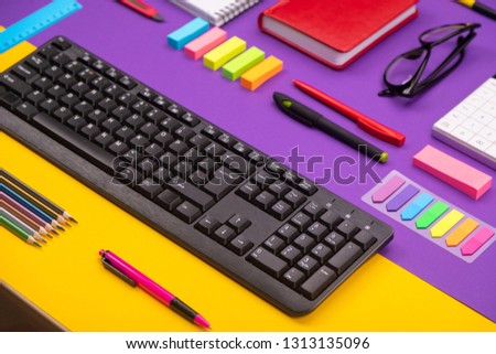 Modern working place with keyboard, diary, pencils, pens and glasses on orange-purple background. Top view