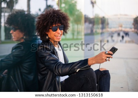 Handsome young black man with afro hairstyle sitting in the street with mobile and skateboard in a sunny city