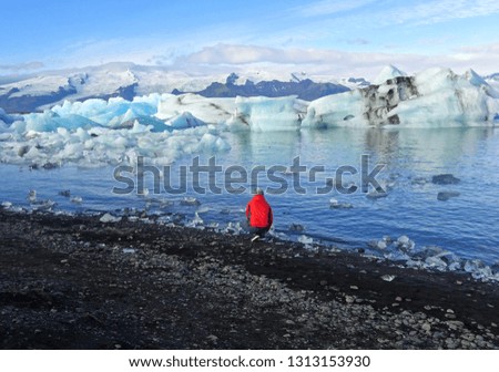                        Man in a bright red jacket taking photos of Jokulsarlon lagoon in Southern Iceland        