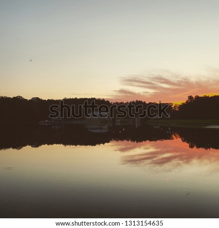 The sun is setting on a lake near a campground.  The reflection of the clouds and the forest are in the lake - the dark is starting to creep into the picture.  