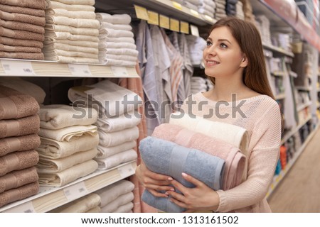 Gorgeous young woman smiling happily, shopping at textile department of a local supermarket. Beautiful female customer buying cotton towels at home goods store, copy space Royalty-Free Stock Photo #1313161502