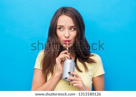people concept - smiling young woman or teenage girl in yellow t-shirt drinking soda from can through paper straw over bright blue background Royalty-Free Stock Photo #1313180126