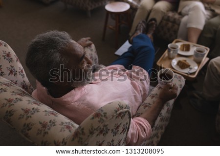 High angle view of senior man having black coffee in living room and sitting on sofa at nursing home