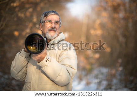 Senior man devoting time to his favorite hobby - photography - taking photos outdoor with his digital camera/DSLR and a big telephoto lens