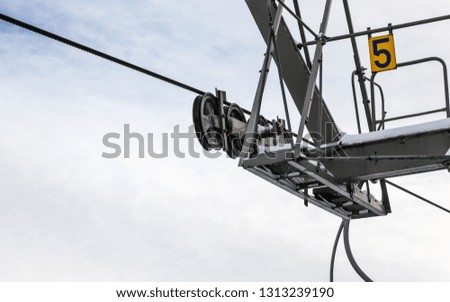 Steel ropes over wheels in mechanism on top of ski lift support pillar, number 5 on yellow plate. Wide banner with space for text left down