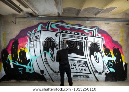 a graffii artist sprays art work of a boom box ghettoblaster on a wall 