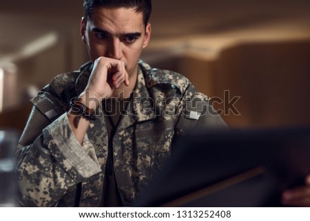 Young sad military officer looking at framed picture with nostalgy. 
