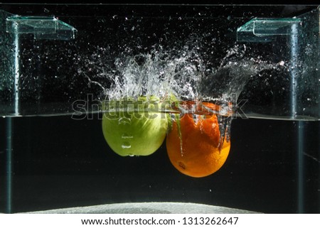 Apple and orange splashing into water on a black background, fishing tank exposed shooting in the studio