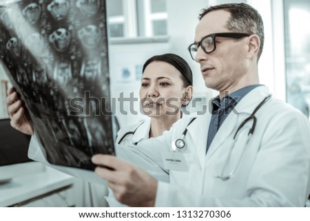 Workmate interestedly looking. Couple of professional doctors attentively reviewing x-ray photo of bone structure of the body