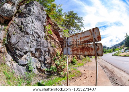 panoramic view of a rusty traffic signal on one side of the road with a huge natural stone wall on a cloudy day
