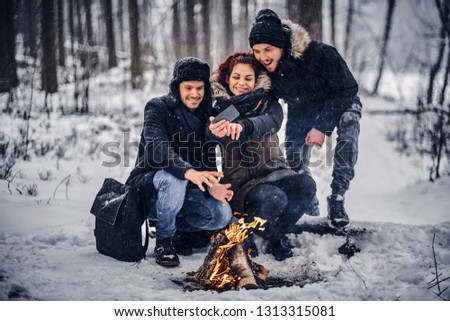 Happy company students doing selfie near the campfire in the winter forest
