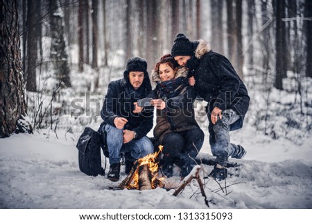 Cheerful friends of travelers do Sefli sitting by the fire in the midst of a snowy forest