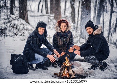 Cheerful company of students basking near a campfire in a snowy forest in winter