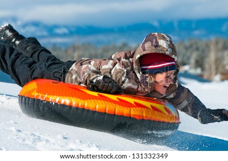 A smiling boy having fun sledding on a tube in the snow.