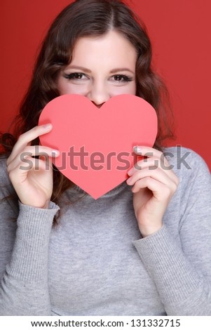 Cheerful girl holding a pink heart on red background on Holiday