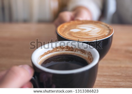 Close up image of a man and a woman clinking two coffee mugs on wooden table in cafe