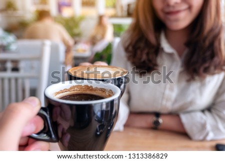 Close up image of a woman clinking coffee mugs to a man in cafe