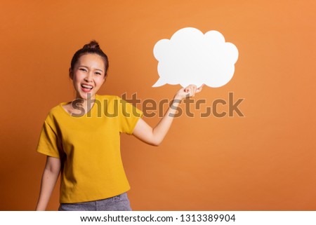 Young Asian woman show text box, speech bubble and copy space over orange background, empty space for text and ads, studio light