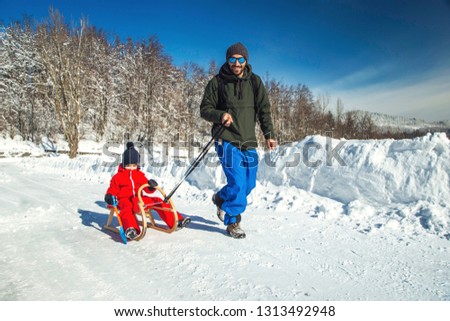     Happy father and hit son enjoying sledding ride. Happy family with sled in winter having fun together. Child sledding. Family driving sled under winter snow. Winter holidays. 