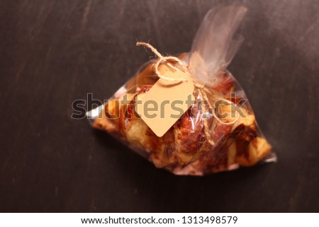 Fresh homemade French croissants with filling in a transparent cellophane bag with a tag on a black table