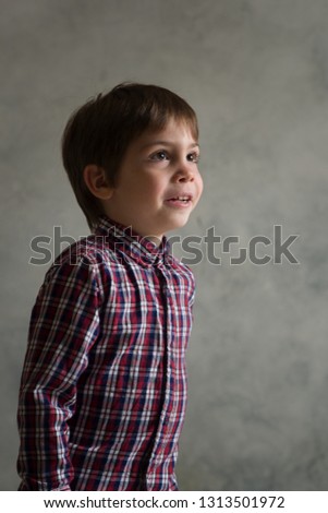 Young boy in plaid shirt sitting in studio on the dark background.