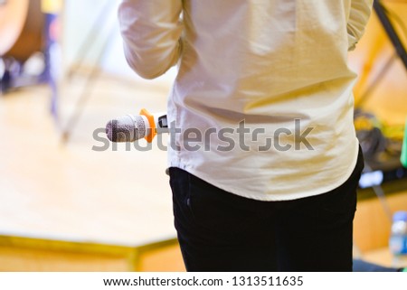 Royalty high quality free stock photo of an unidentified asian man holding a microphone, wearing a white shirt, looking from behind with copy space for text or advertising or background. He is a MC