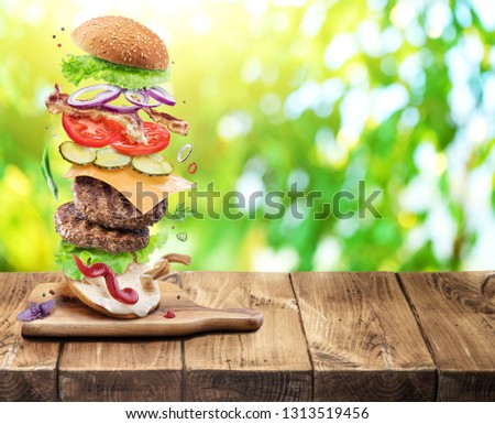 Hamburger ingredients falling down one by one to create a perfect meal. Colorful conceptual picture of burger cooking. Green nature background.
