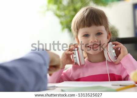 child in headphones sitting at home table and looking into camera portrait.