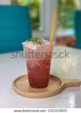 Glass of ice strawberry juice with soda on white table.