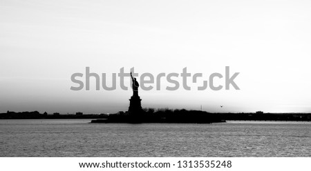 Nice backlight of a panoramic view of American symbol Statue of Liberty silhouette in New York, USA at sunet. High key black and white image.